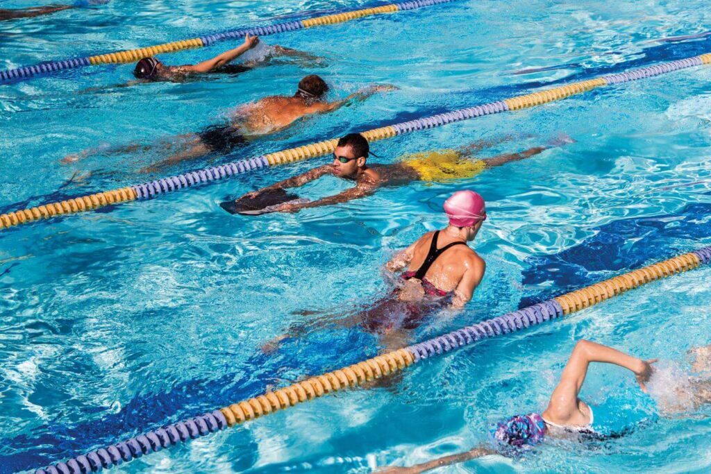 Group of people taking swimming lessons in a pool, practicing different techniques.