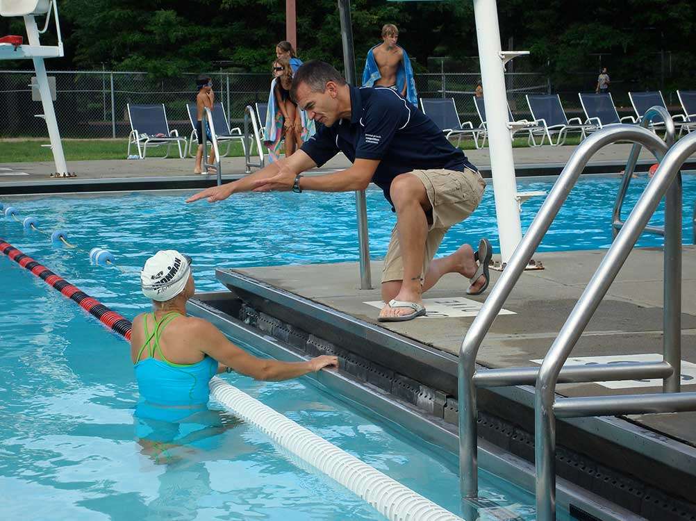 Swimming coach standing at the poolside, giving instructions to a student in the water