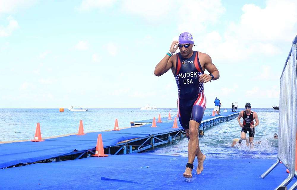 Triathlete transitioning from the swimming portion of the race, emerging from the water and starting to run toward the next stage.